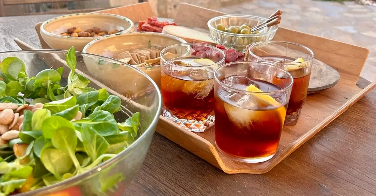 glasses of vermut sitting on a wooden tray with accompaniments